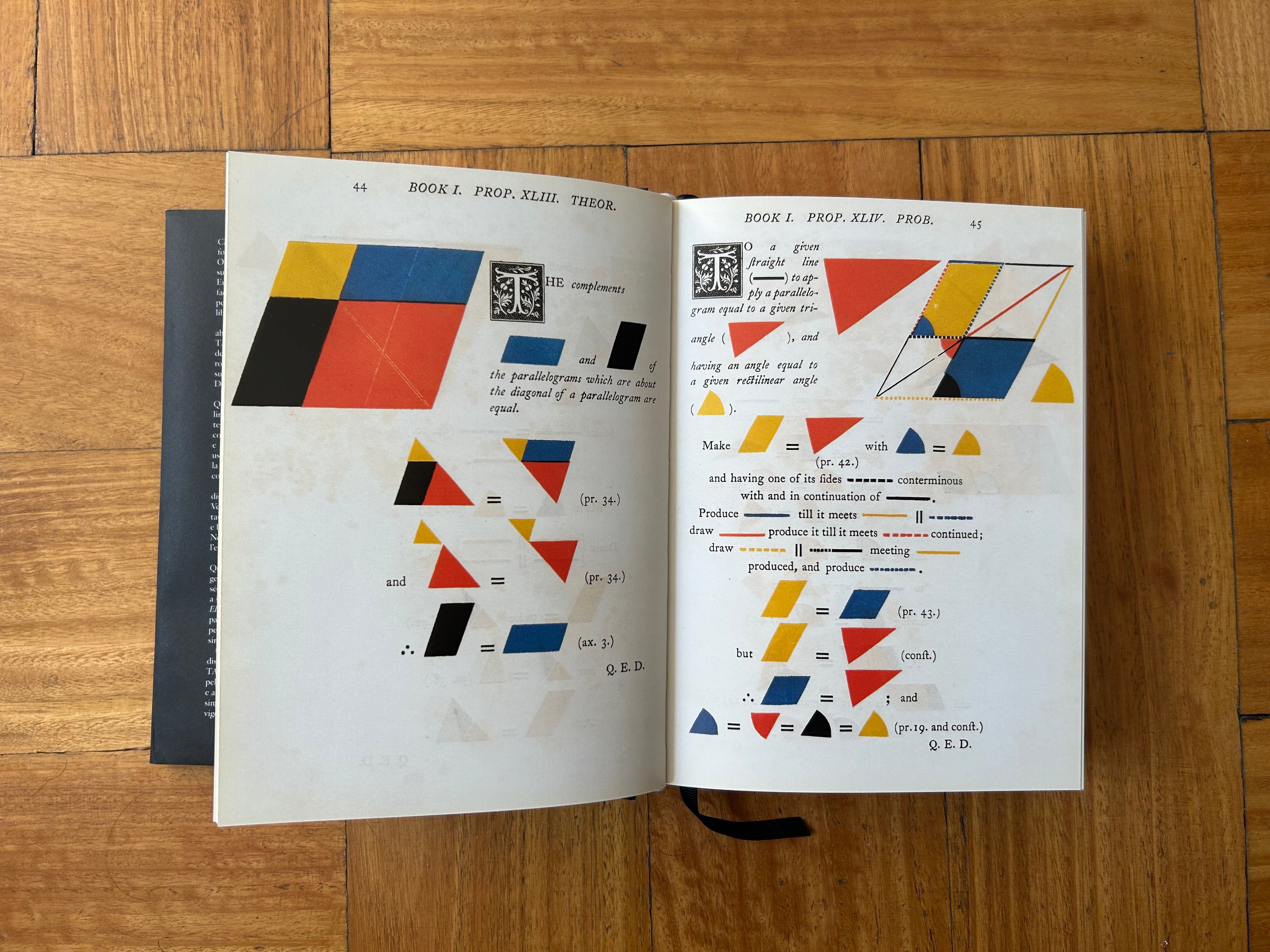 Photo of book open showing geometric diagrams of quadrilaterals, against a wooden floor.